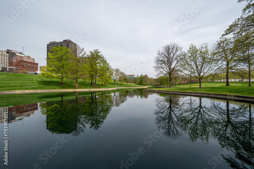 Buildings of Saint Louis, Missouri reflected in reflecting pool in Gateway Arch National Park on overcast April morning.