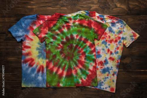 Three bright tie dye T-shirts on a wooden background.