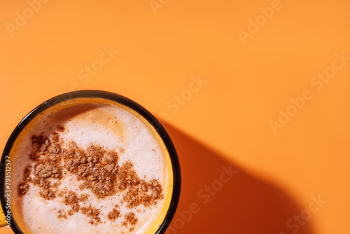 Yellow mug with coffee and cinnamon on an orange background.