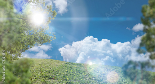 春・夏　煽りで見上げた丘・土手の野原の坂道　さわやかな晴天の青空と雲の背景壁紙 太陽の日差しと光レンズフレア　アウトドア・夏休み・祝日・行楽・観光・旅行・ゴールデンウィーク・ウォーキング・散歩のイメージ素材 © tenpadasi