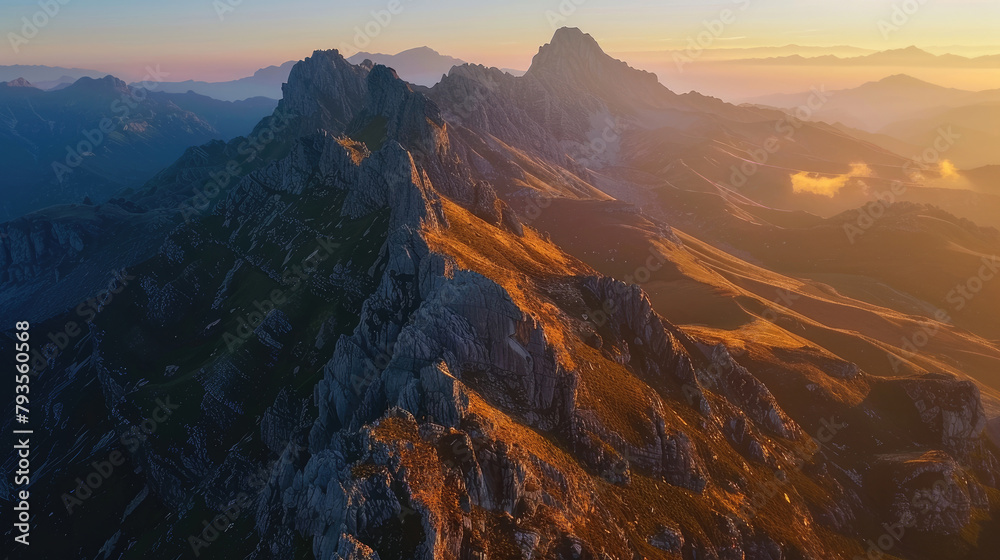 Aerial view of a mountain range at sunrise, the peaks illuminated with golden light against the shadowed valleys