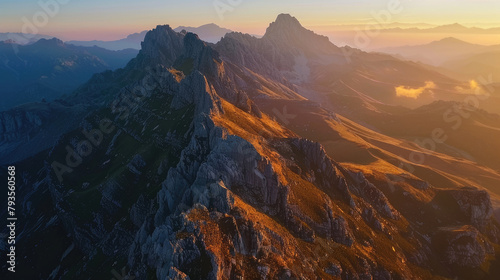 Aerial view of a mountain range at sunrise, the peaks illuminated with golden light against the shadowed valleys