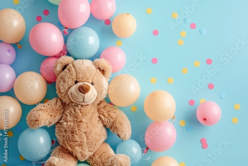 Smiling brown teddy bear holding heap of colorful balloons on light blue table background. Pastel color. Closeup. Congratulation concept. Top down view.