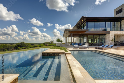A large, modern home with an expansive pool and patio area in the Texas countryside. The house has multiple levels of windows overlooking the beautiful blue sky and green grass. © Kien