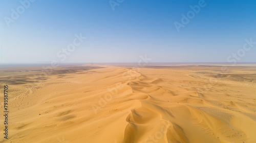 Aerial view of a vast desert with sand dunes rippling towards the horizon under a clear blue sky