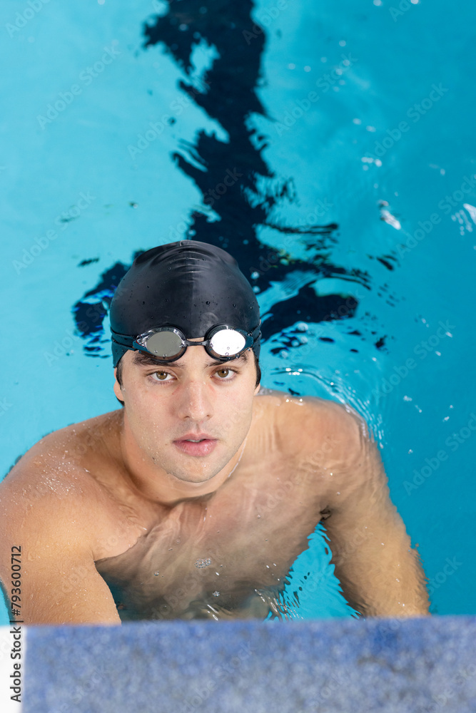 Caucasian young male swimmer with dark hair training indoors in swimming pool