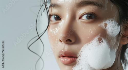 Korean beauty model with flawless skin, using facial wash to swirl thick white foam on her face, closeup of the washing process.