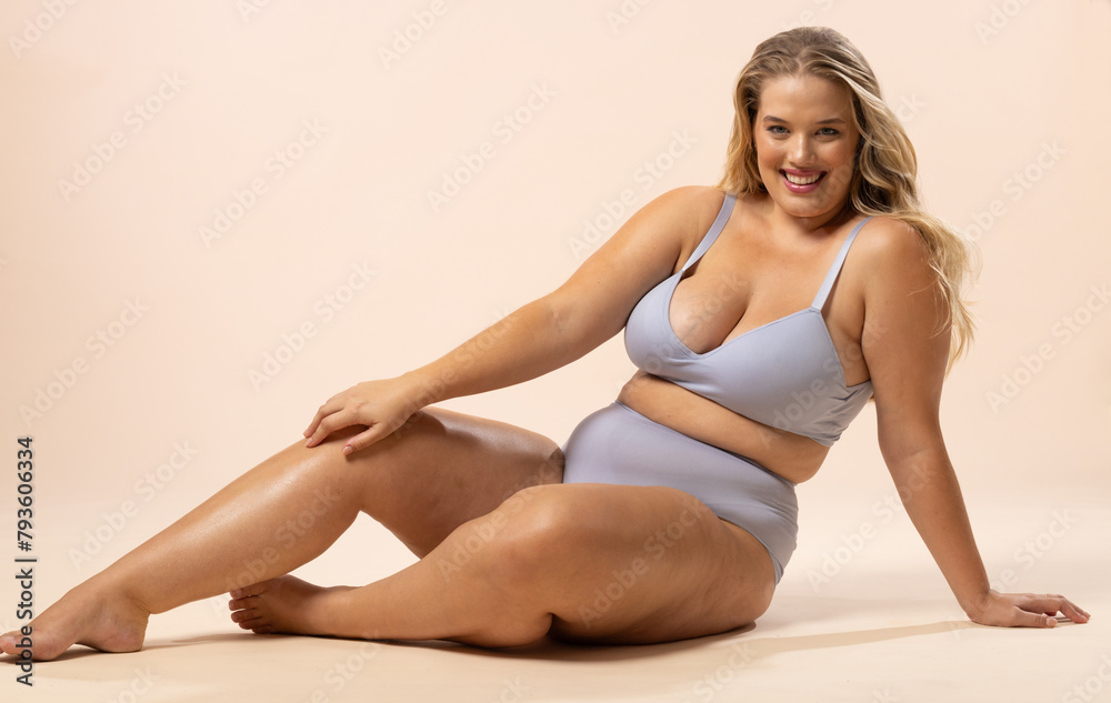 Caucasian young female plus size model sits on floor in light blue sportswear, copy space Caucasian young female plus size model sits on floor in light blue sportswear, copy space