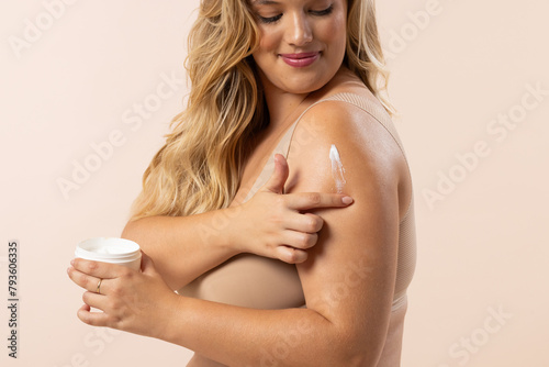 Caucasian young female plus size model applies lotion to her arm