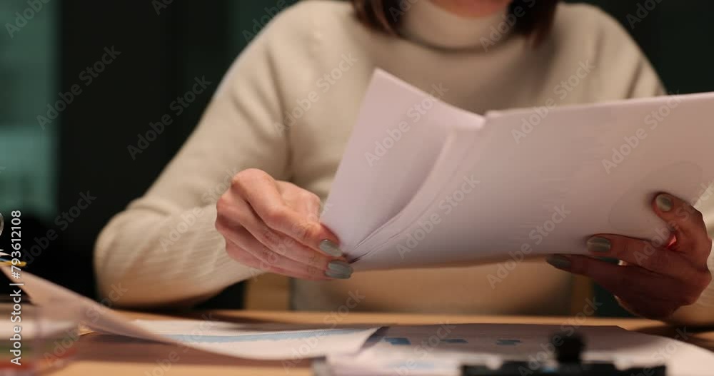 Woman reads financial documents in the evening at workplace