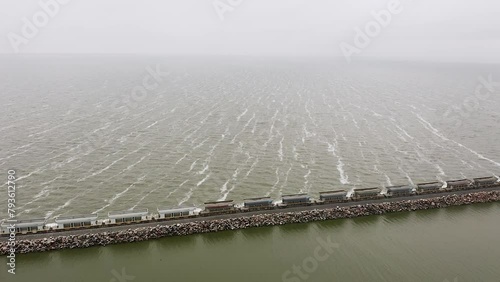 Wide aerial pan of long freight train on straight track by sea in Argentina photo