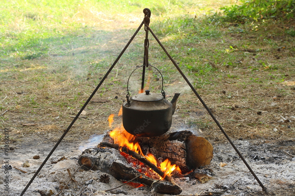 A smoked aluminum kettle hangs on a tripod over a fire. A smoked aluminum kettle hangs on a tripod over a fire.
