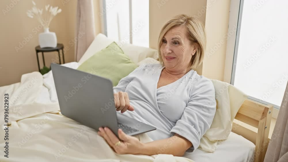 A smiling woman using a laptop in a cozy bedroom setup, exuding comfort and leisure. A smiling woman using a laptop in a cozy bedroom setup, exuding comfort and leisure.