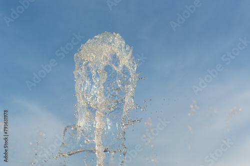 Fountain jet in close-up. A sparkling stream of the purest water against the blue sky. The concept of coolness cooling and water saving. The flow of water spray is seen from below. Abstract background