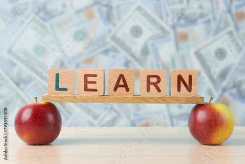  Image symbolizing the value of education, with LEARN spelled out on wooden blocks perched on apples, set against a backdrop of assorted currency notes