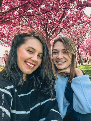 Obraz na płótnie two happy girlfriends taking selfie under blooming sakura tree w salonie