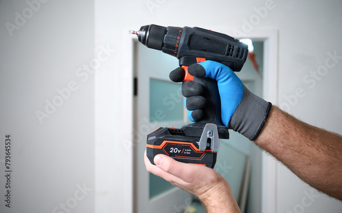 Construction worker holding electric cordless screwdriver in hand at construction site. Accessories for assembling, install furniture, repair home. Home renovation, electric tool for job. Crop view.
