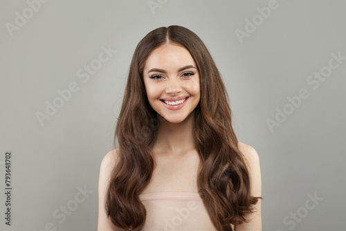 Brunette young female model with healthy hair, makeup and shiny clear skin posing against gray studio wall background. Facial treatment, cosmetology, hair care and beauty woman concept