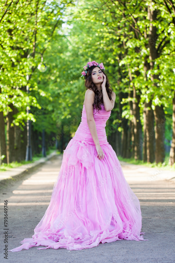 Fashionable healthy woman with makeup and long wavy dark brown hairstyle with flowers on head in spring park outdoor