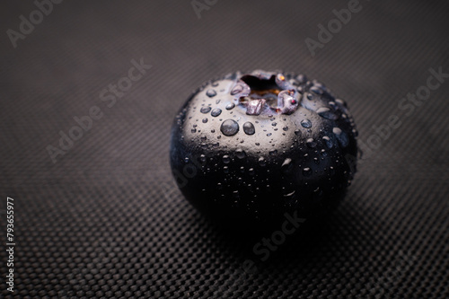 One blueberry covered with water drops on black background. Very detailed macro shoot with copy space