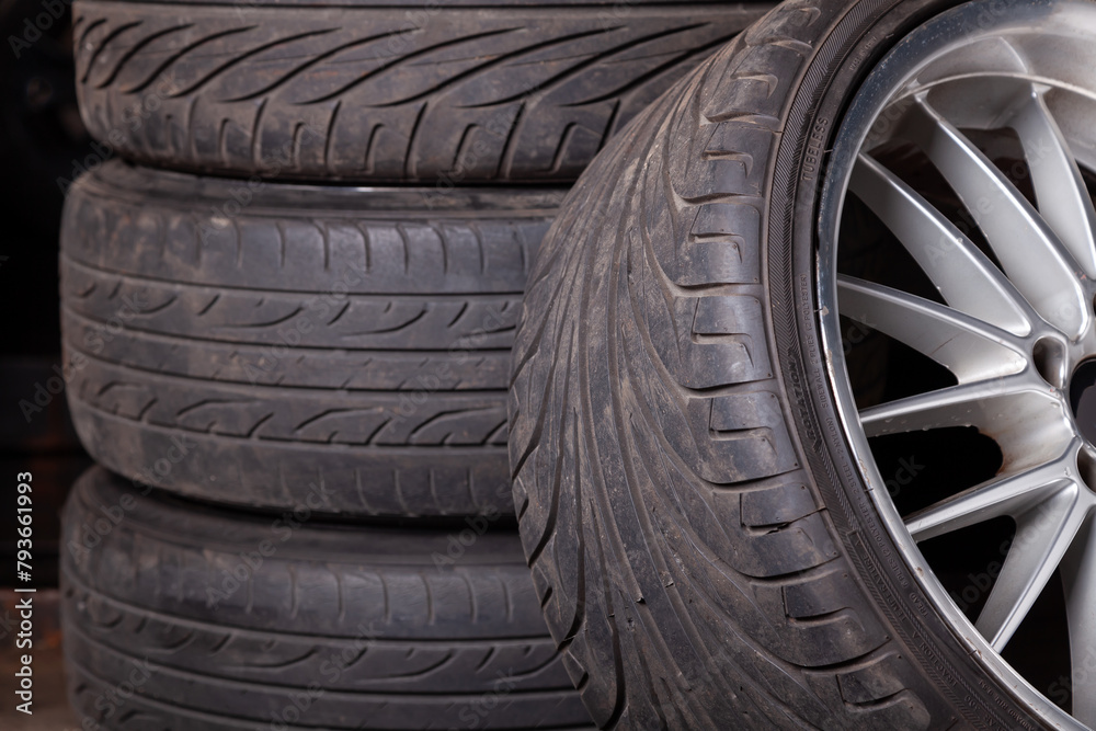 Automobile composition made up stack of tires and wheel with shiny disc in a car service before seasonal replacement or after breaking through.