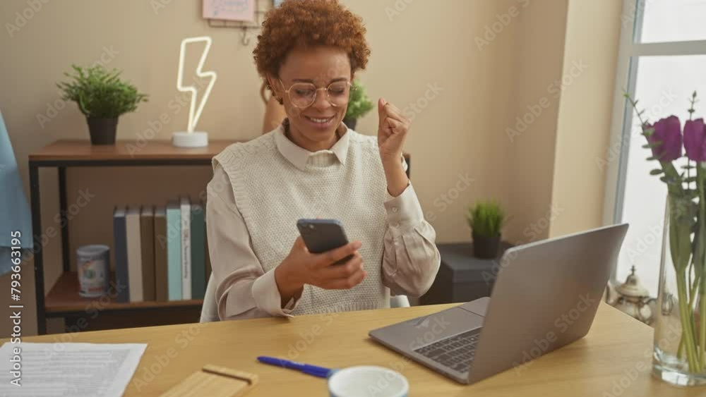 African american woman using smartphone with laptop in a cozy home office setup, expressing positivity. African american woman using smartphone with laptop in a cozy home office setup, expressing positivity.