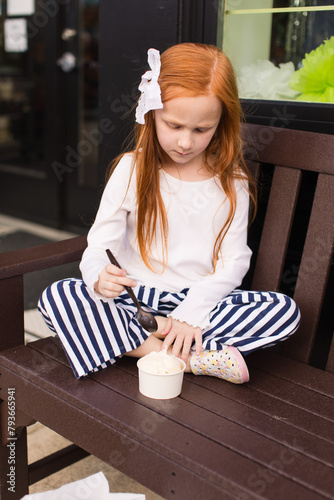 Redhead girl eats ice cream on bench photo