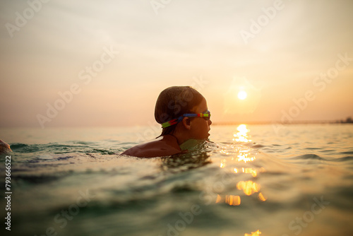 Calm child with goggles swimming at ocean sunset photo