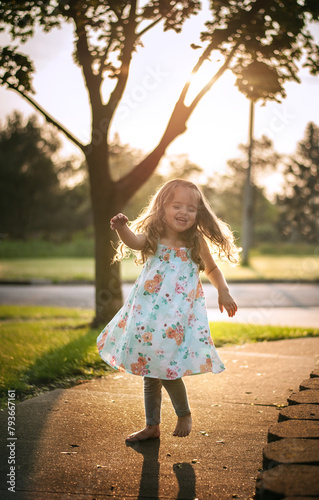Beautiful happy little girl with long curls dancing outdoors in summer photo