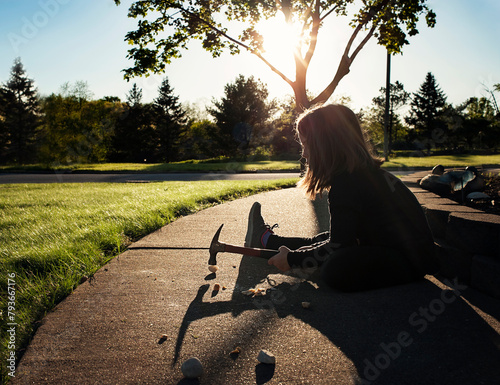 Young girl smashing rock with hammer on sidewalk in summer photo