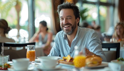 Man at table smiles while eating breakfast with food, juice, and plate