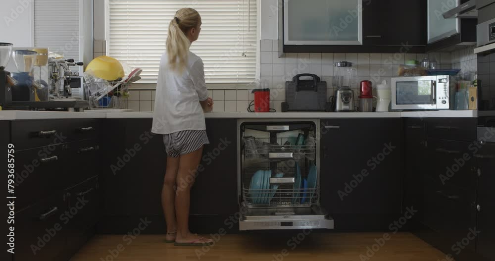 A mother stands by the dishwasher in a kitchen, overseeing her young children as they energetically play around her. A mother stands by the dishwasher in a kitchen, overseeing her young children as they energetically play around her.