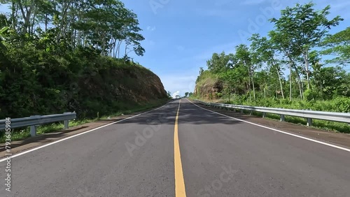A beautiful curved road with hills on the side and blue sky in the background. in Blitar, East Java, Indonesia. JLS stand for Jalur Lintas Selatan (South Cross Lane)  photo