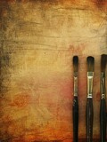 Three paintbrushes on a rustic brown textured backdrop.