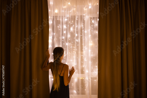 Woman standing near window with Christmas illumination. Christmas holidays concept.