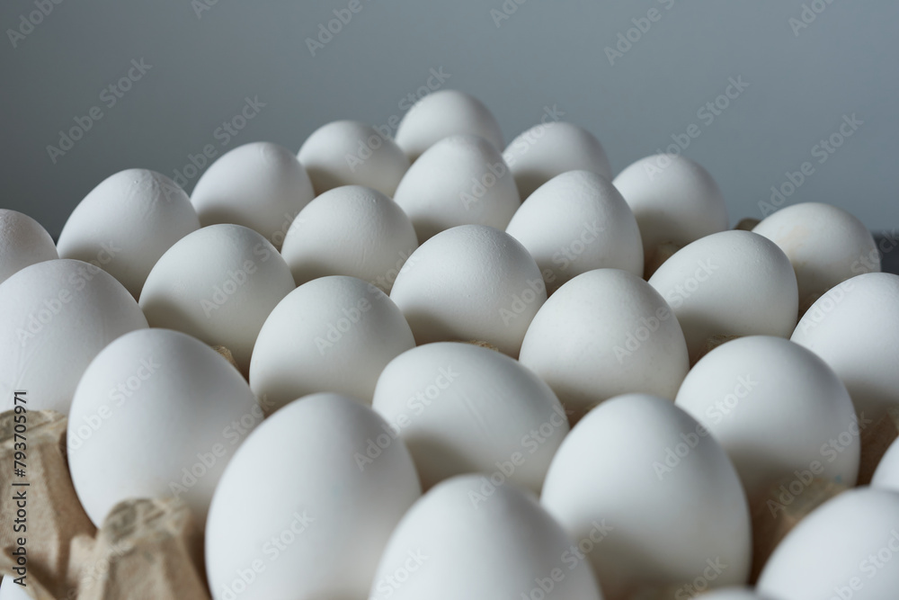 White eggs in a cardboard box on a gray background. Close-up. White eggs in a cardboard box on a gray background. Close-up.