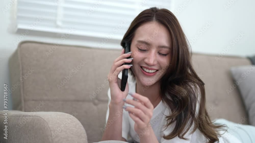 A radiant young woman enjoys a lively conversation on her phone, comfortably lounging on a sofa in a living room. A radiant young woman enjoys a lively conversation on her phone, comfortably lounging on a sofa in a living room.
