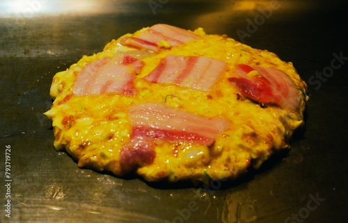 Okonomiyaki being cooked.Okonomiyaki with pork and eggs