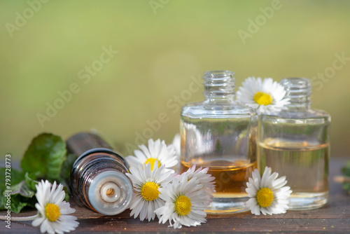 bottles of essential oil and daisies with fresh mint leaf on a wooden table  outdoors © coco