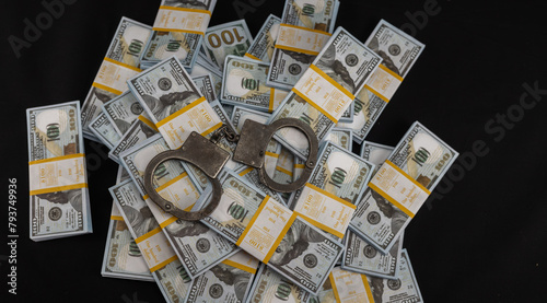 Handcuffs lie on stacks of hundred dollar bills on a black background. View from above. Money and handcuffs on a black background. Concept of punishment for financial fraud.