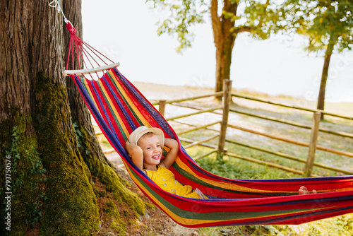 A laughing child lies in a bright hammock outdoors with his hands behind his head.