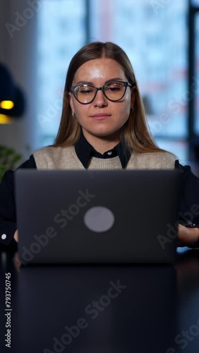 Lady in glasses opens laptop, prints something and closes it. Long-haired woman puts off glasses and lays her head on hands. Blurred backdrop. Vertical video