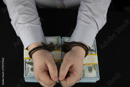Top view of handcuffed male hands lying on stacks of hundred dollar bills. On a black background, men's hands in handcuffs against a background of dollars. a man was arrested for bribery.