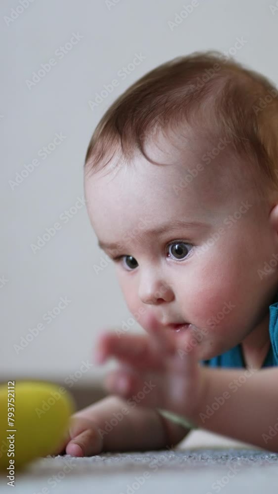 Active baby waving hands lying on the floor. Caucasian child trying to reach a toy in front of him. Light backdrop in blur. Vertical video Active baby waving hands lying on the floor. Caucasian child trying to reach a toy in front of him. Light backdrop in blur. Vertical video