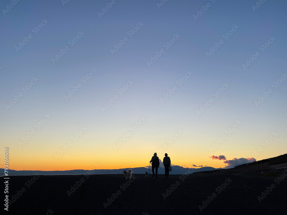 湘南海岸の夕日が沈む茅ヶ崎で犬と散歩をする人のシルエット