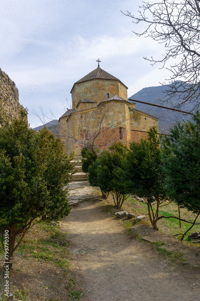 Fototapeta premium Ateni Sioni. Earthen road to the church through coniferous trees. Mountains on background. Georgia.