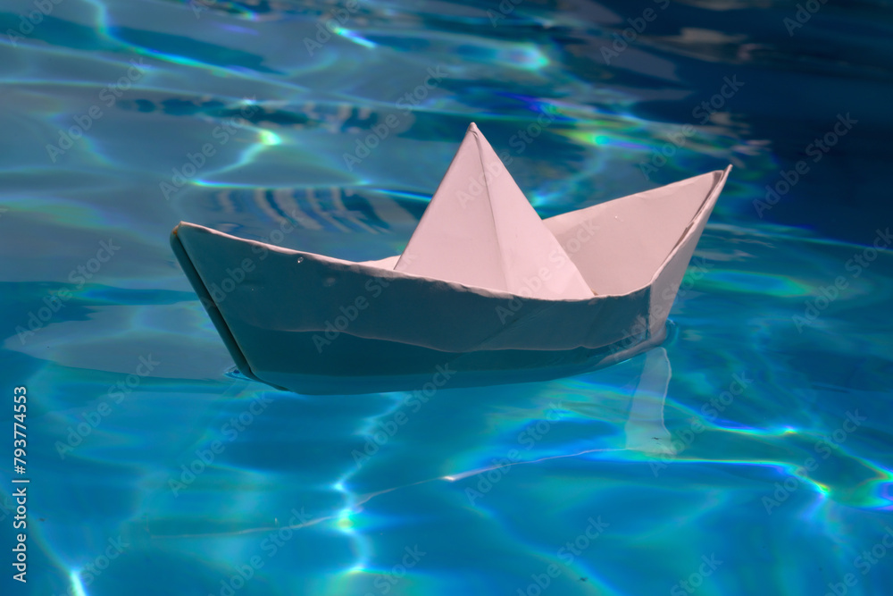 Paper boat on blue water background. Paper boat sailing on blue water surface. Concept of tourism, travel dreams vacation holiday, dreaming traveling, sailing adventure. Paper craft and origami.