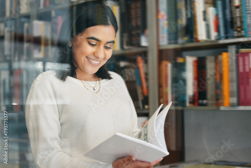 Woman, student and reading in college library with smile for research, learning and education. Happy, female person, and university bookshelf with novel, literature or biography for studying