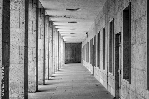 A vanishing perspective view of a modern arcade with evenly spaced columns and ceiling lights. Black and white image.