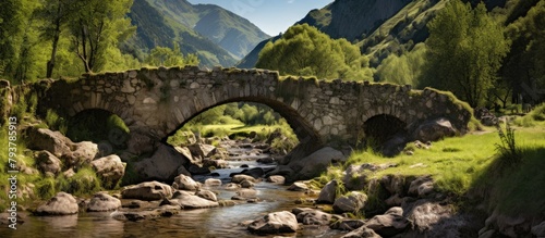Stone bridge spans across valley stream with distant mountains